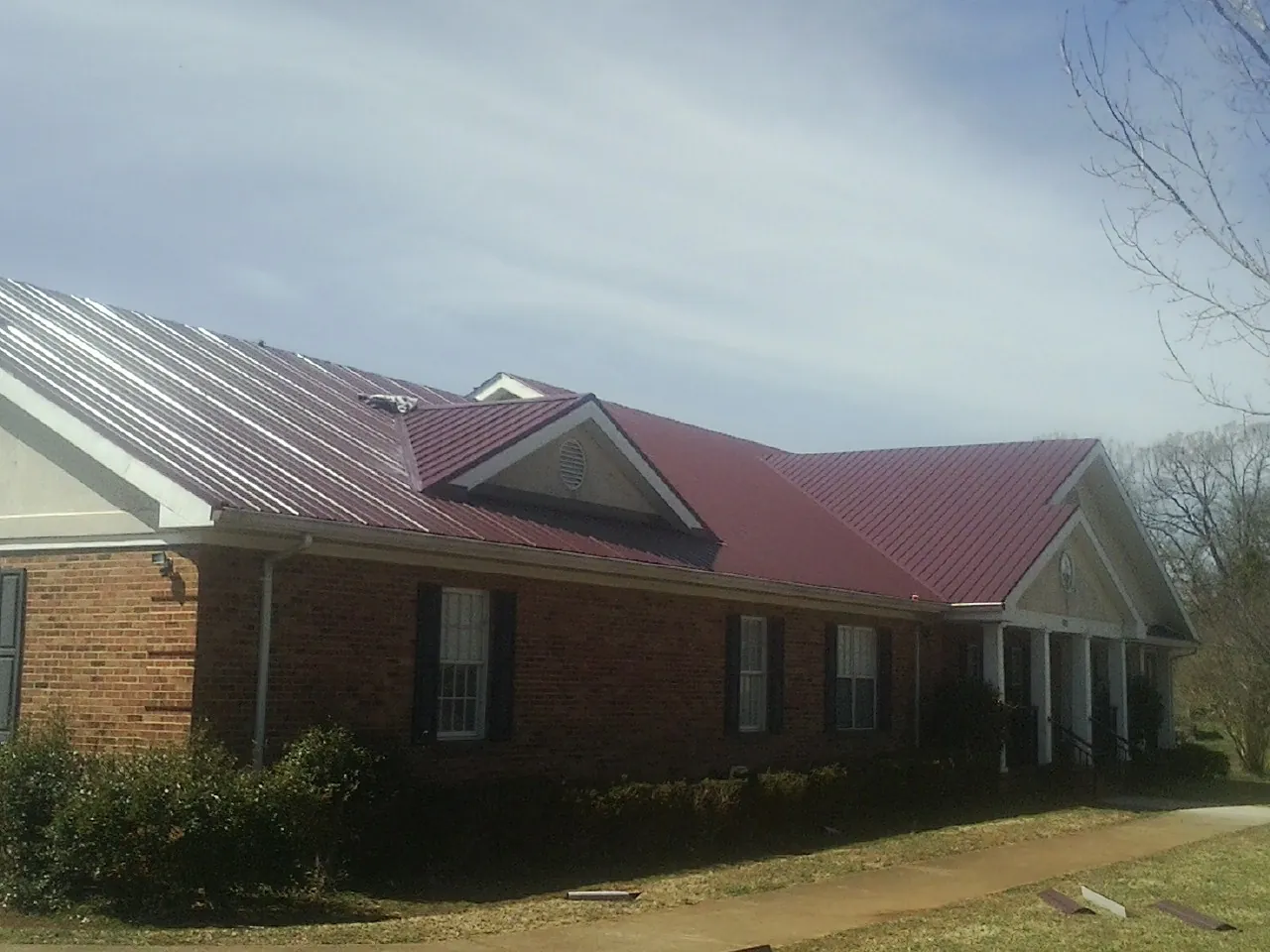 Red metal roof with gabled entries on a long brick building, from a Hail Damage Roof Repair job in Napanoch