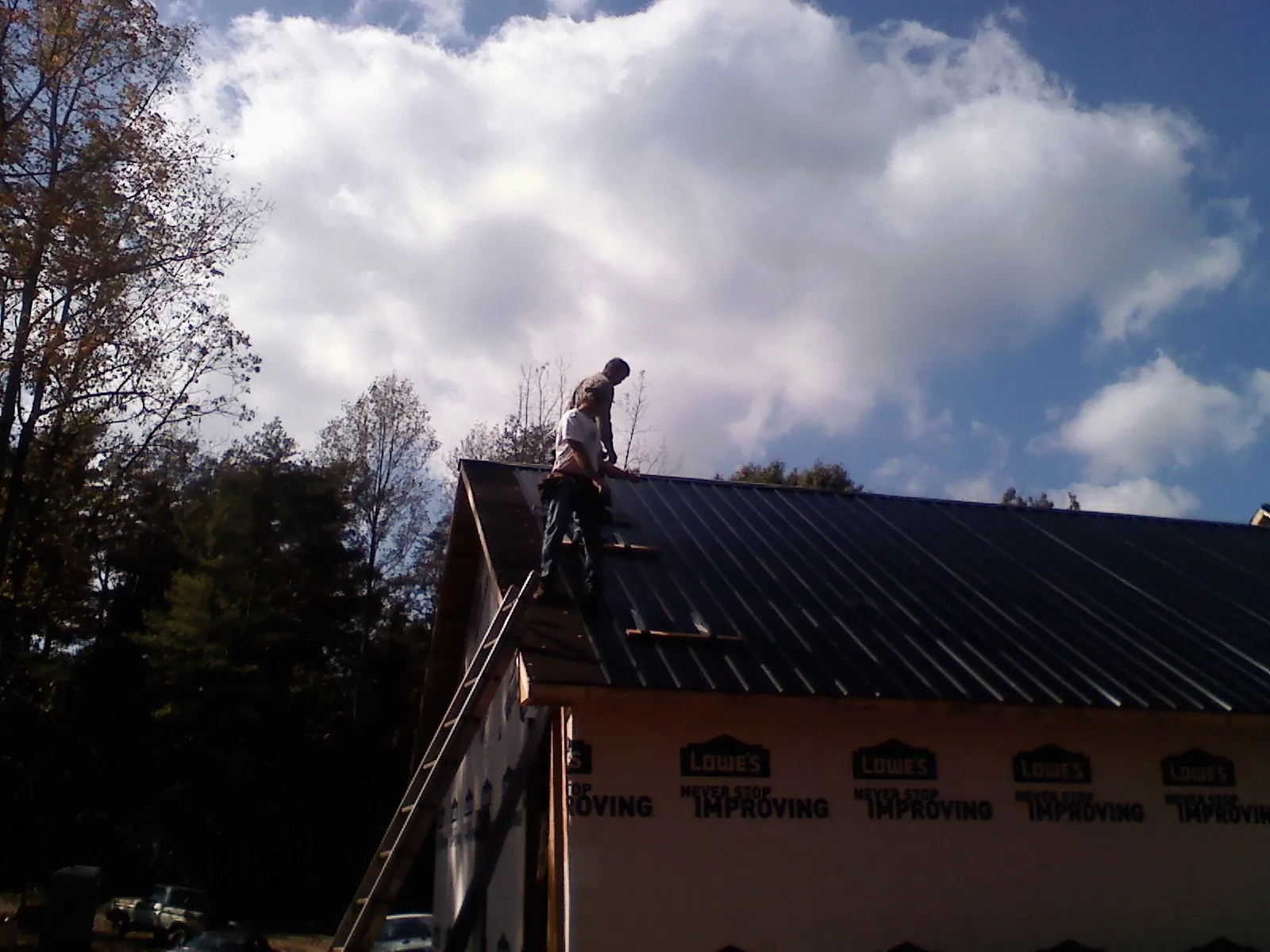Roofer fastening dark metal panels high against a cloudy sky, from a Roof Inspection job in Napanoch