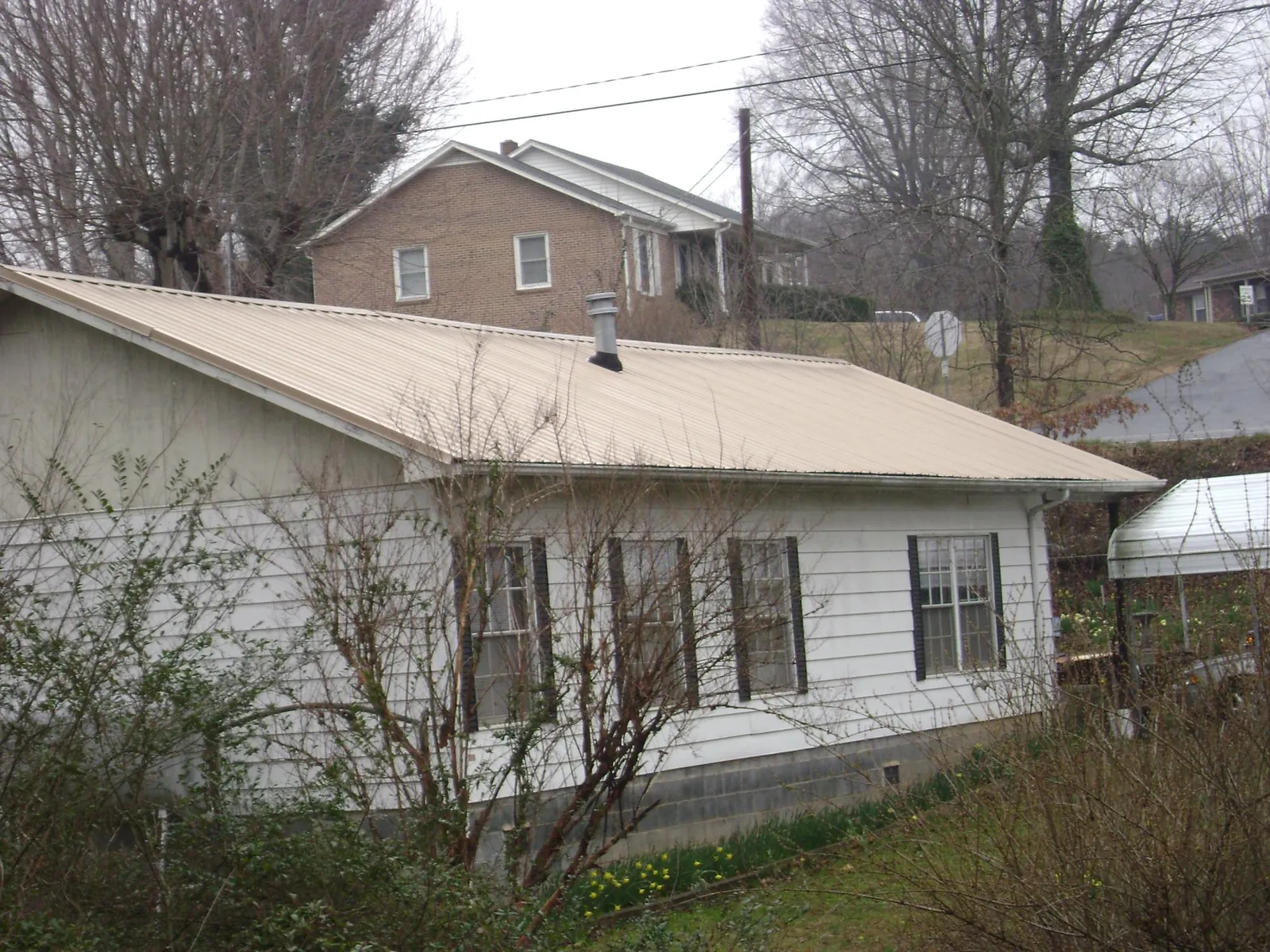 Tan metal roof on a white sided house set into a hillside — Commercial Roofing by Roofing Brothers in Napanoch